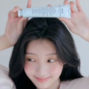 Person holding a skincare product above their head with a plain background