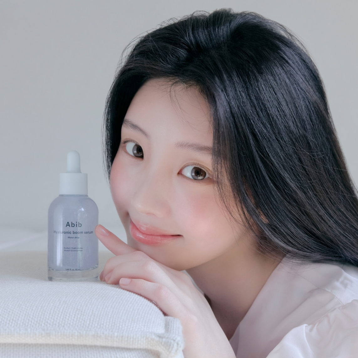 Woman holding a bottle of Abio skincare product on a neutral background