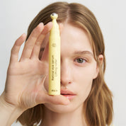 Person holding a yellow eye serum product near their face against a plain background