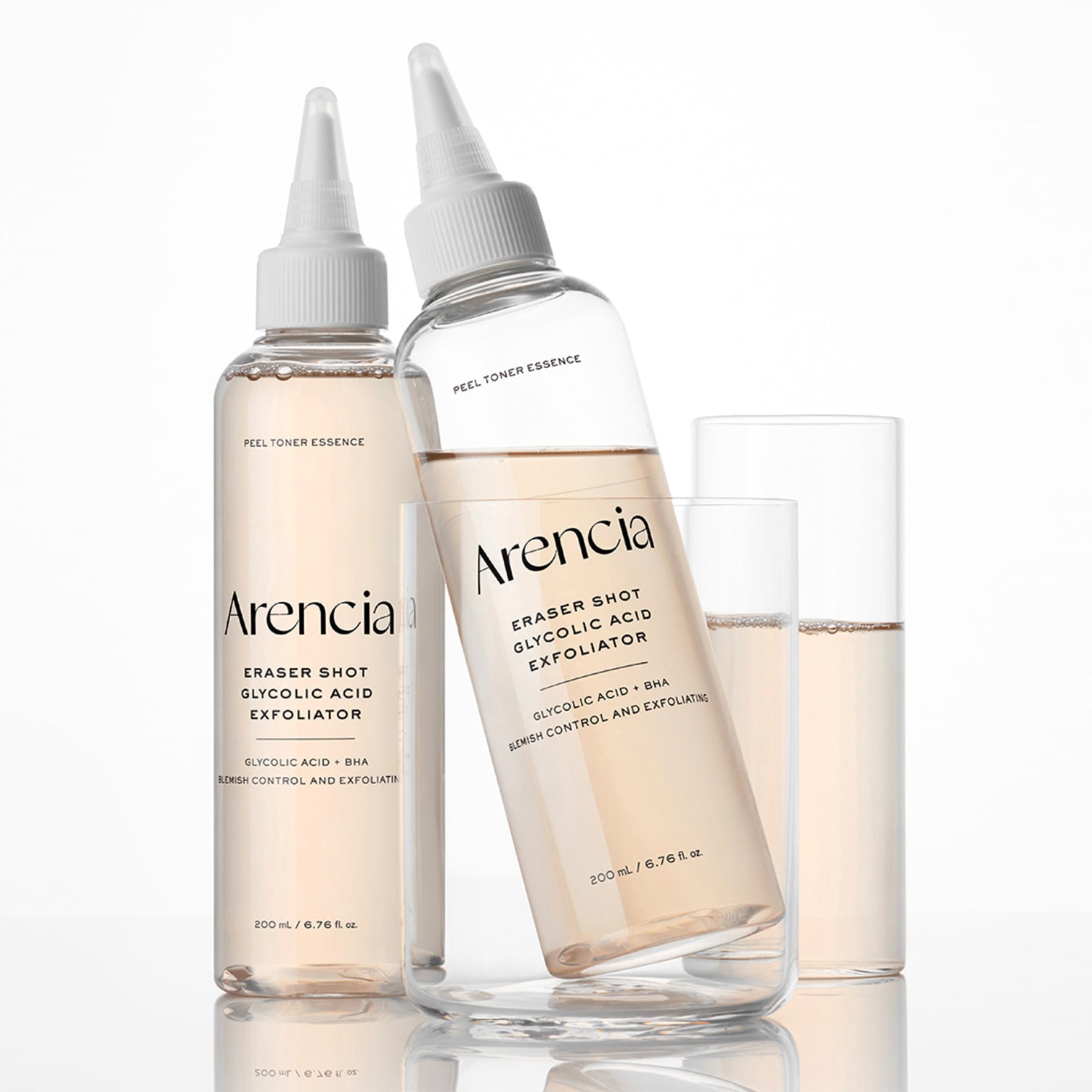 Two clear ARENCIA Eraser Shot Glycolic Acid Exfoliator with white dropper-style caps and two clear drinking glasses on a white background. The bottles are labeled Arencia Eraser Shot Glycolic Acid Exfoliator and Peel Toner Essence.