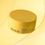 A yellow jar of Arencia Retinal Boosting Eye Mask on a matching yellow background with abstract curved lines.