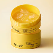 Two open yellow jars of Arencia Retinal Boosting Eye Mask stacked on a warm cream background, showing the translucent gel patch product inside.