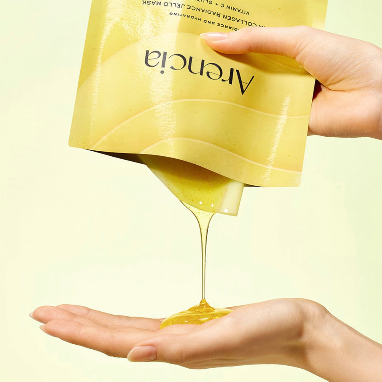 A hand holds a yellow ARENCIA Vita Collagen Radiance Jello Mask to pour a thick, glossy golden-yellow gel into another hand, against a pale yellow background.