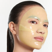 A close-up of a woman wearing a ARENCIA Vita Collagen Radiance Jello Mask on her face, with her dark hair pulled back, against a plain light background.