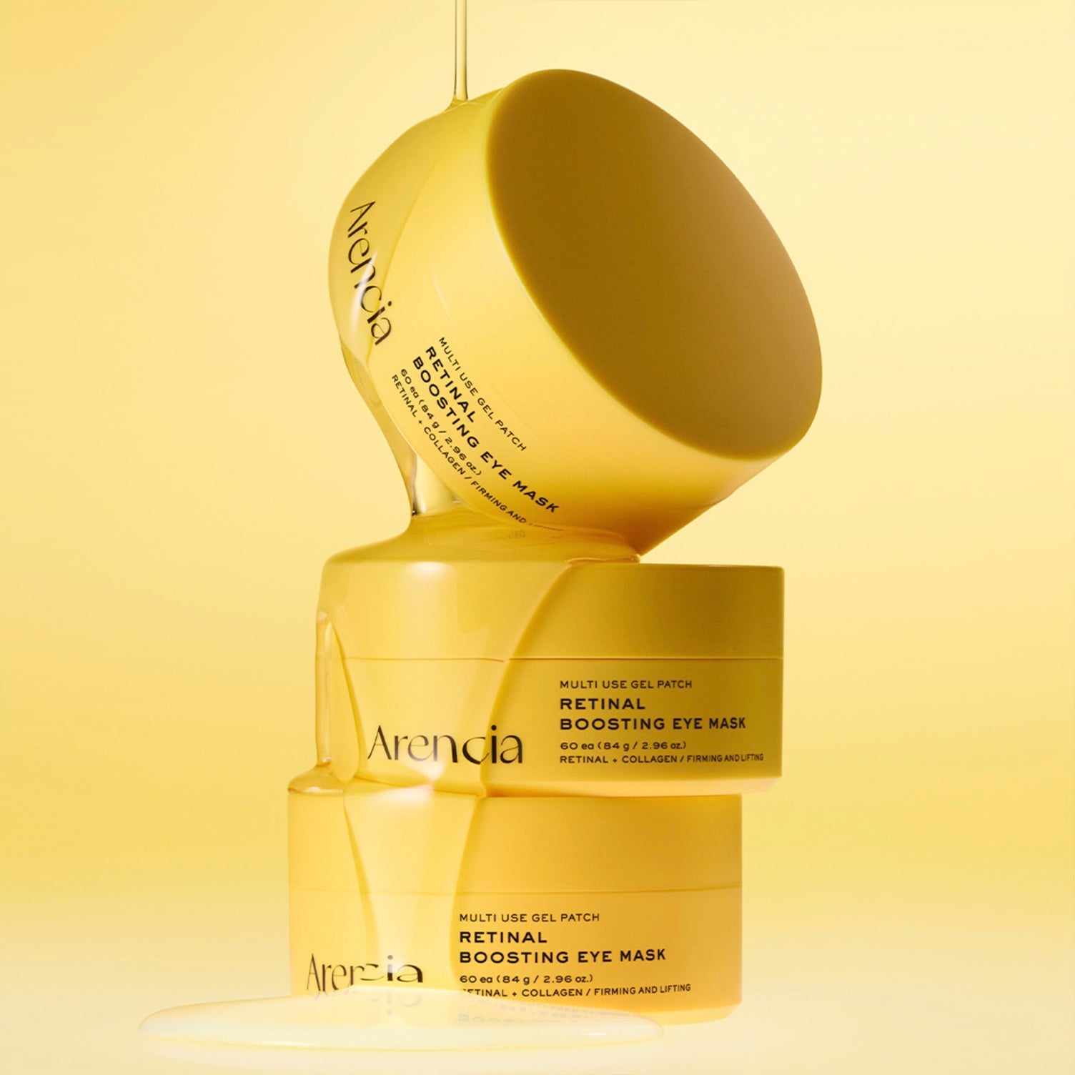 Three yellow cosmetic jars of ARENCIA Retinal Boosting Eye Mask and tipped over on a pale yellow background, with gel visibly dripping from the top jar.