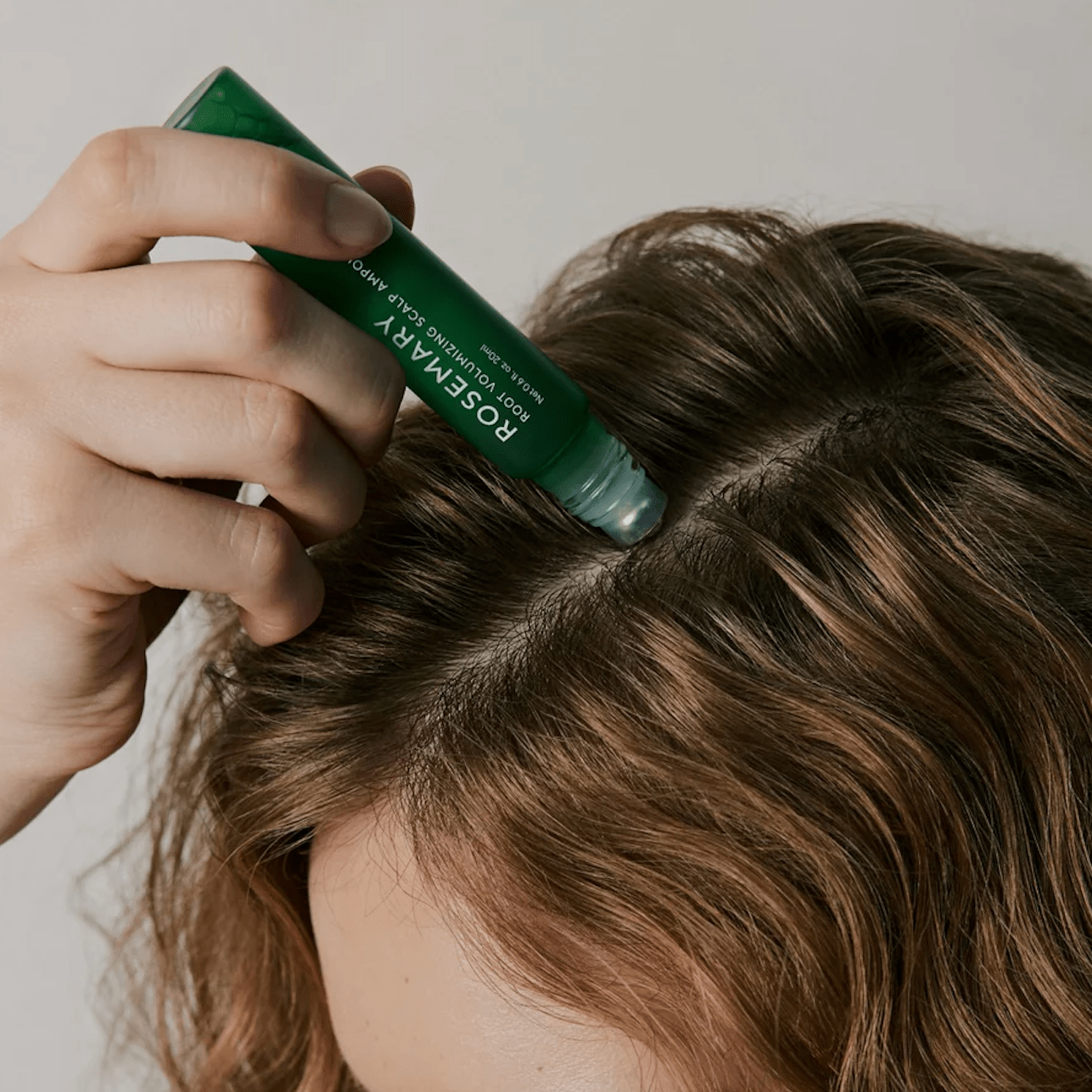 Person applying a AROMATICA Rosemary Root Volumizing Scalp Ampoule labeled 'Rosemary' to their hair.