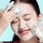 Woman applying a facial cleanser with a light blue background