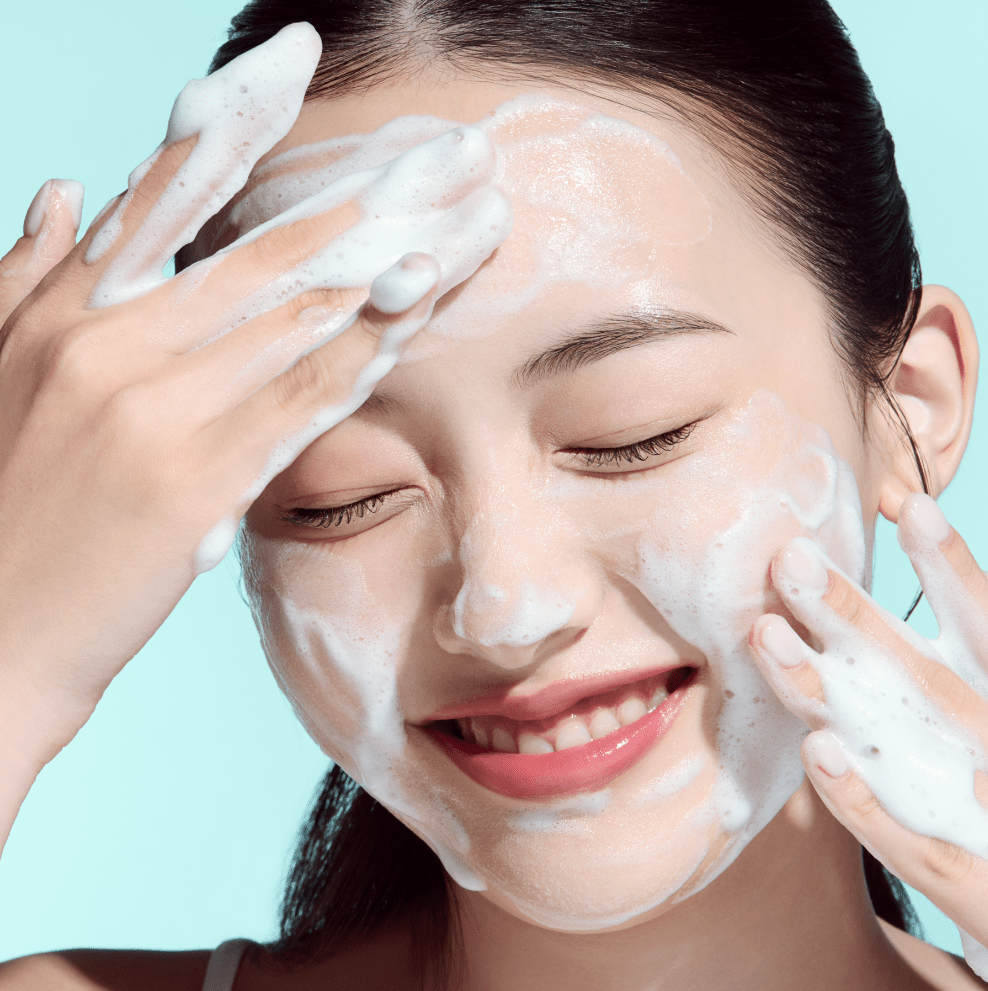 Woman applying a facial cleanser with a light blue background