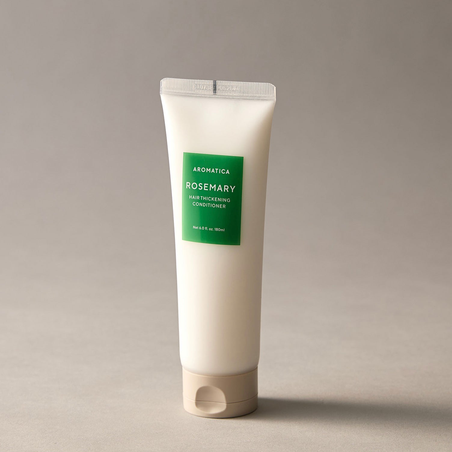 Tube of Aromatica Rosemary hair thickening conditioner on a gray background