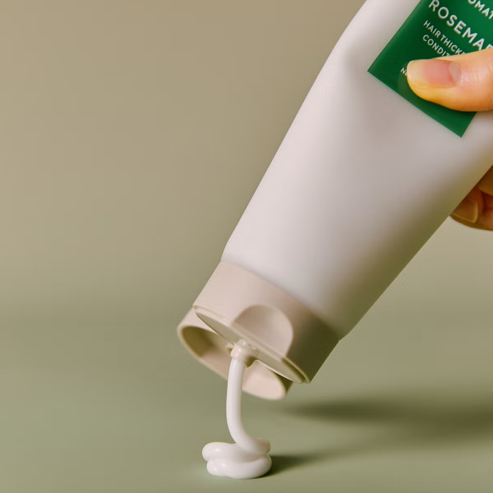 Hand holding a bottle of AROMATICA Rosemary Hair Thickening Conditioner with a visible pump.