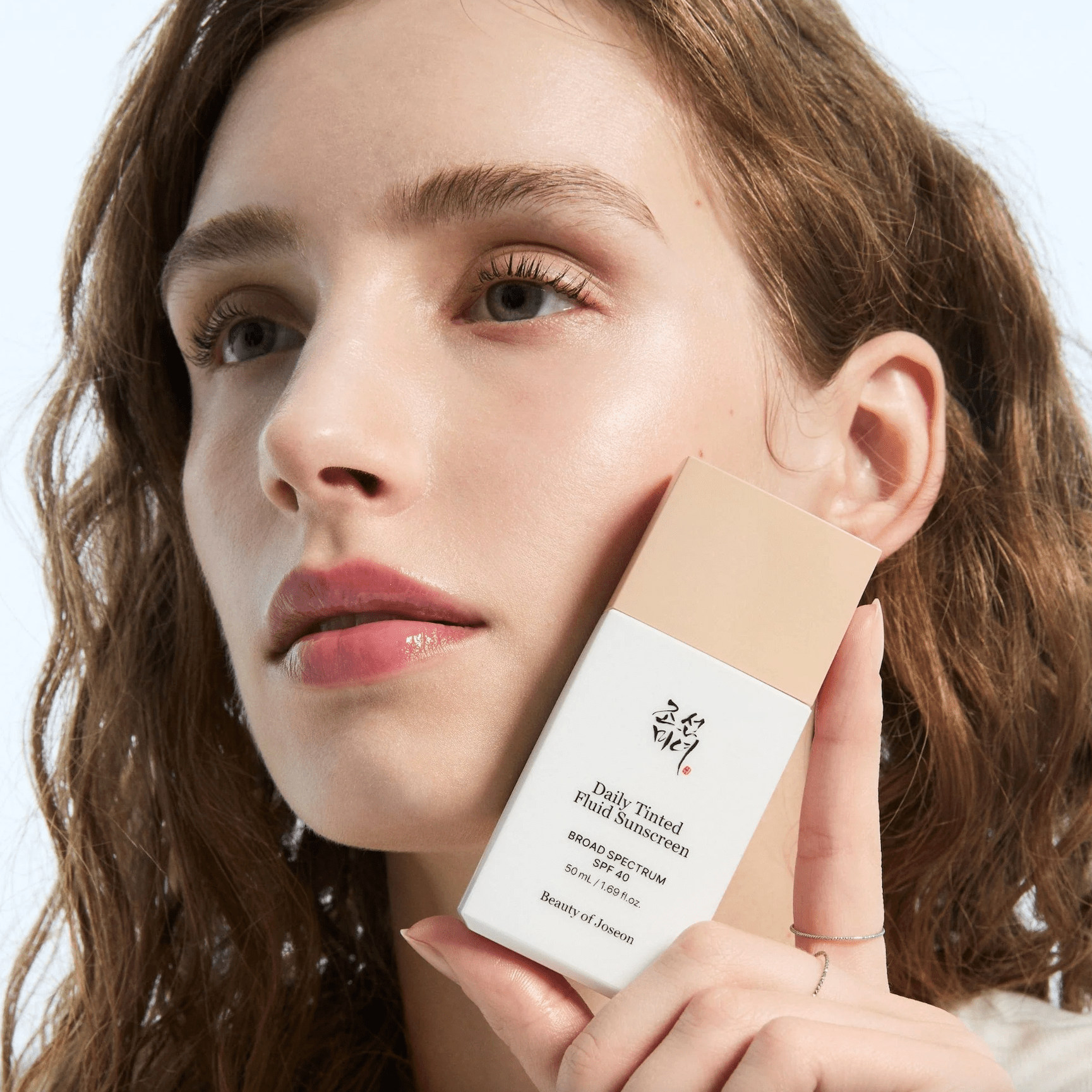 Woman holding a bottle of BEAUTY OF JOSEON Daily Tinted Fluid Sunscreen SPF 50ml