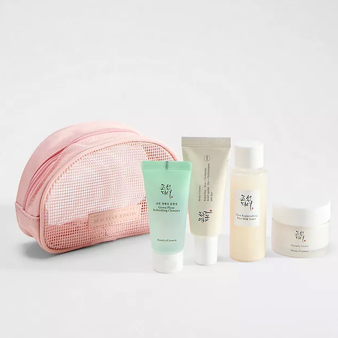 A pink mesh cosmetic pouch with four skincare bottles and tubes from Beauty of Joseon, arranged on a clean white background.