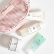 A flat-lay arrangement of Beauty of Joseon Glow Skin Essential Kit (4-Piece Gift Set). on a white background, featuring a pink mesh cosmetic pouch and four white and mint green bottles and jars from the brand Botulose.