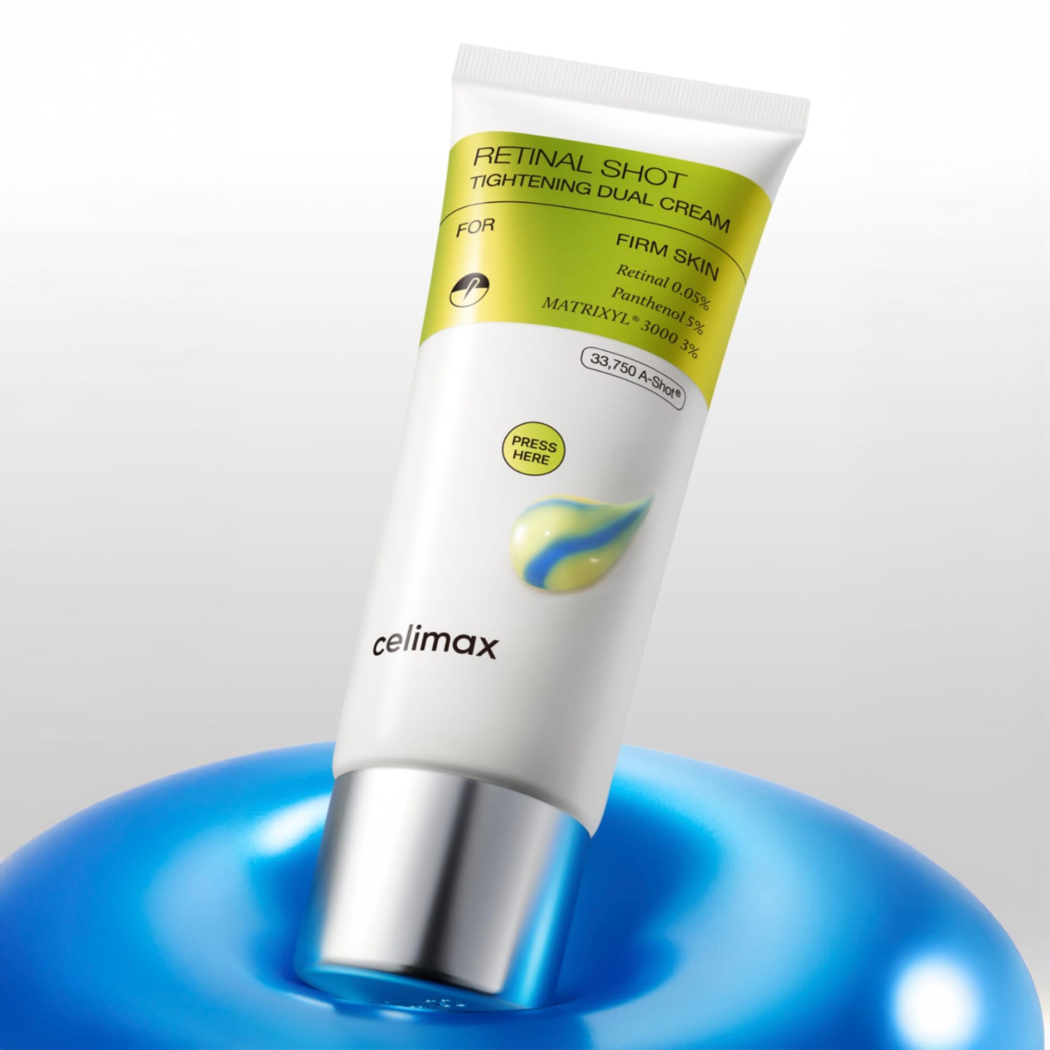 A white tube of CELIMAX The VITA-A Retinal Shot Tightening Dual Cream (50 ml) with a silver cap, standing upright on a glossy blue surface against a light gray background.