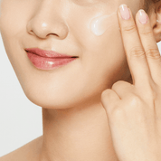 Woman applying COSRX Advanced Snail 92 All In One Cream to her face with a neutral background