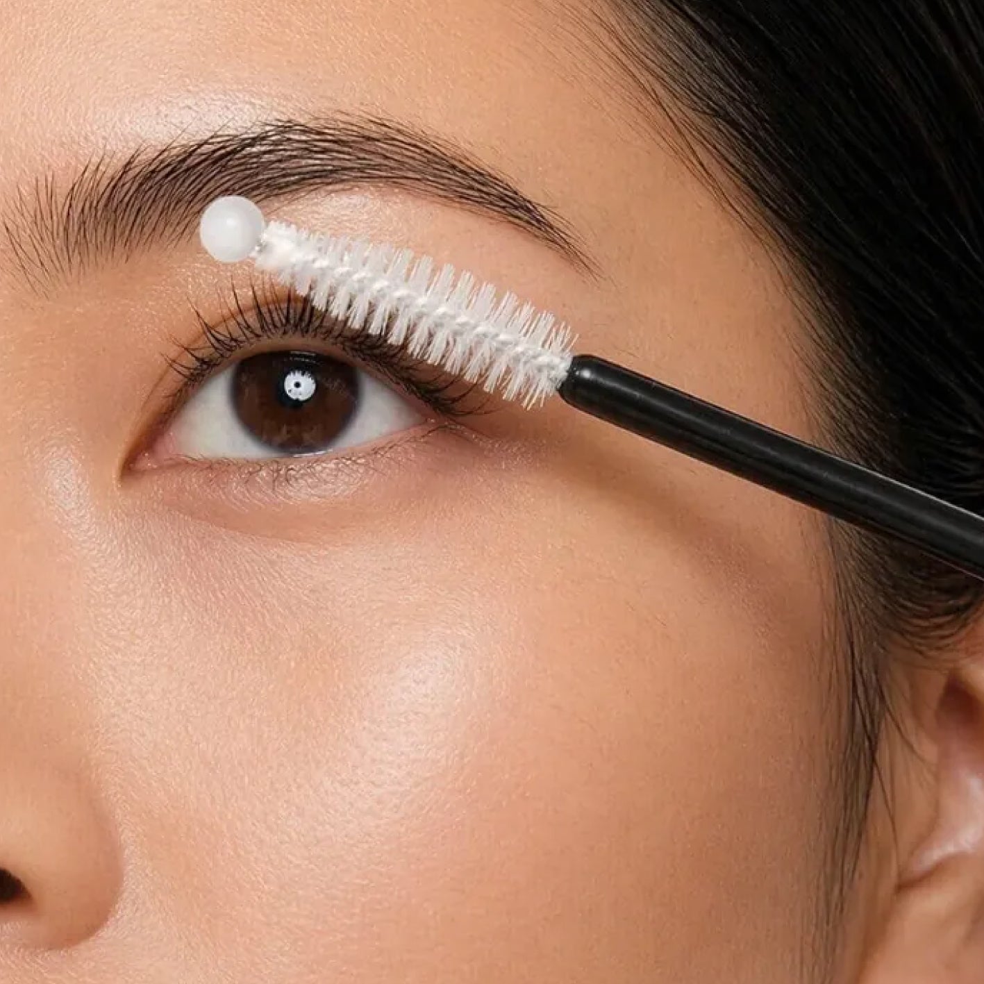 Person applying eyelash gel to their eye with a brush
