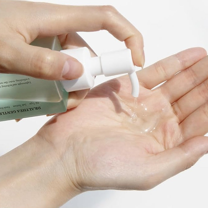 Hand holding a bottle of DR. ALTHEA Gentle Pore Cleansing Oil with a close-up of the liquid being dispensed.