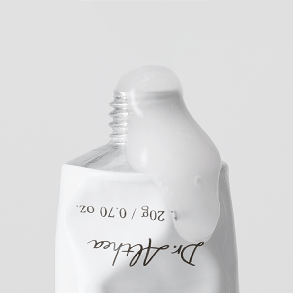 A close-up of a white squeeze tube with a clear cap, showing a glossy white product dripping from the top. The tube has black text reading Dr althea.