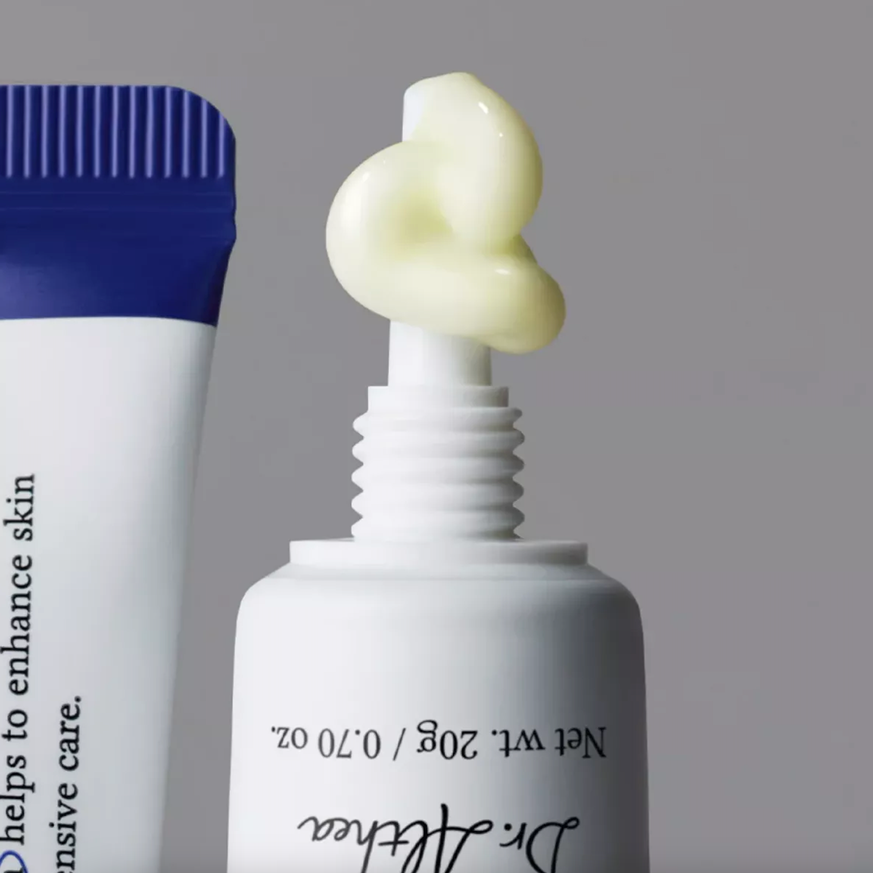A close-up of a DR. ALTHEA Pure Retinol 0.15% Cream with pale yellow cream piped onto the nozzle, next to a blue-and-white tube, on a soft gray background. The front tube shows the brand name Dr.