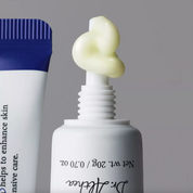 A close-up of a DR. ALTHEA Pure Retinol 0.15% Cream with pale yellow cream piped onto the nozzle, next to a blue-and-white tube, on a soft gray background. The front tube shows the brand name Dr.
