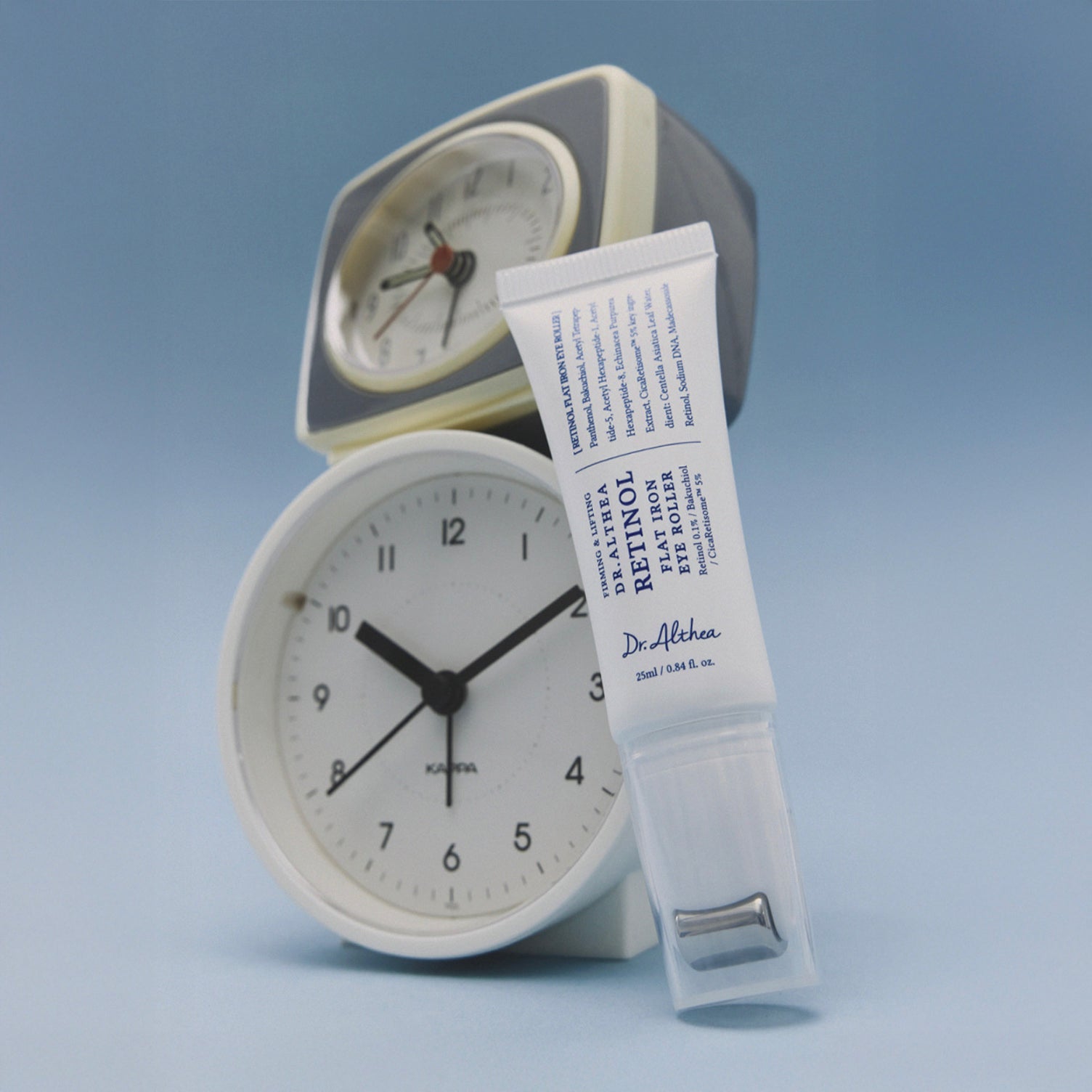 DR. ALTHEA Retinol Flat Iron Eye Roller standing in front of clocks with light blue background