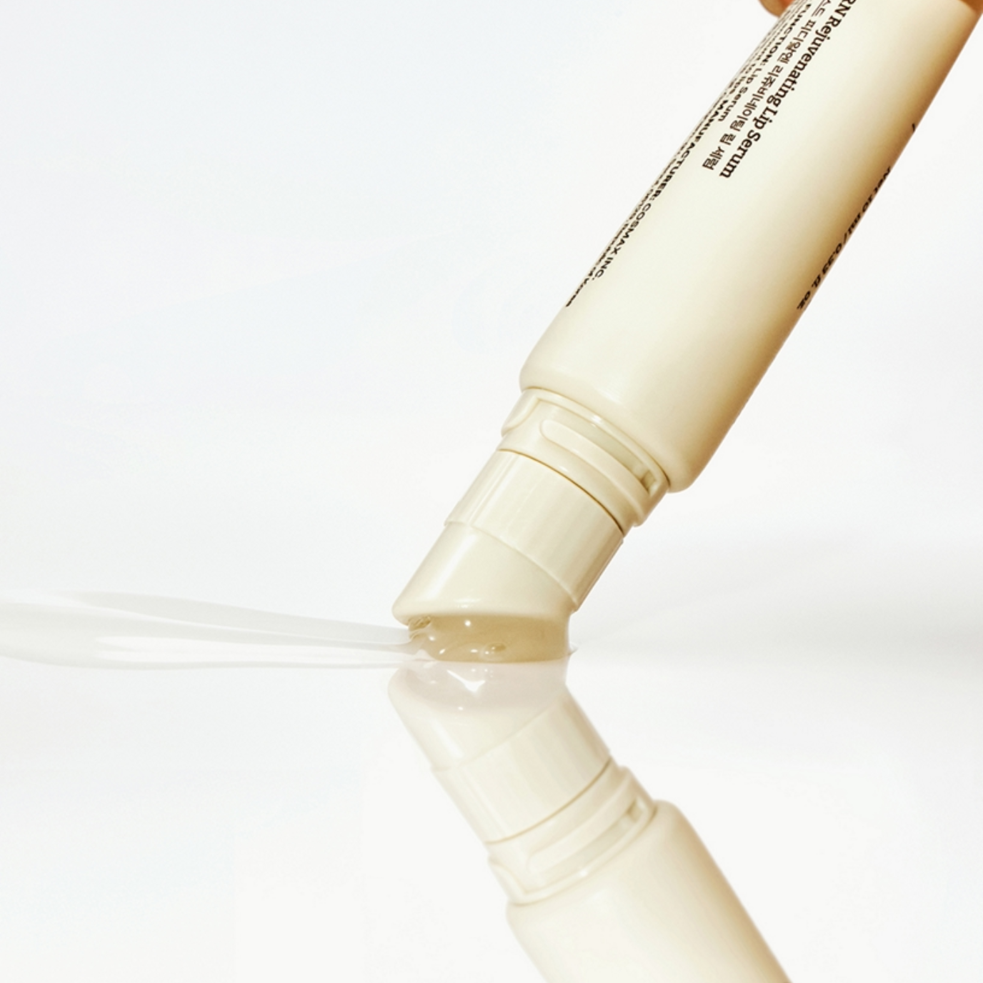 A close-up of a Dr. Reju-All Advanced PDRN Rejuvenating Lip Serum (10ml) tipped over, dispensing a clear gel or liquid onto a glossy white surface with a reflection below.