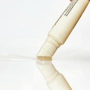 A close-up of a Dr. Reju-All Advanced PDRN Rejuvenating Lip Serum (10ml) tipped over, dispensing a clear gel or liquid onto a glossy white surface with a reflection below.