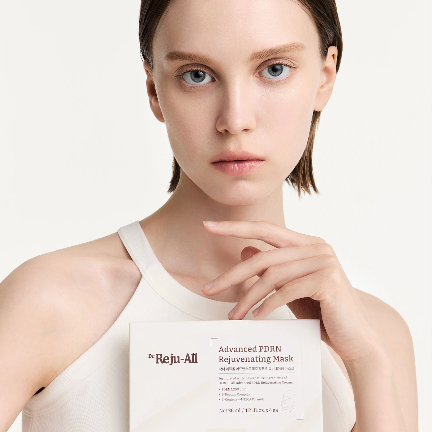 A close-up of a model holding a sheet mask package labeled Dr. Reju-All Advanced PDRN Rejuvenating Mask against a clean white background.