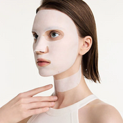 A woman with short brown hair wears a Dr. Reju-All Advanced PDRN Rejuvenating Mask covering her face and neck, with one hand touching her collarbone area, against a clean white background.