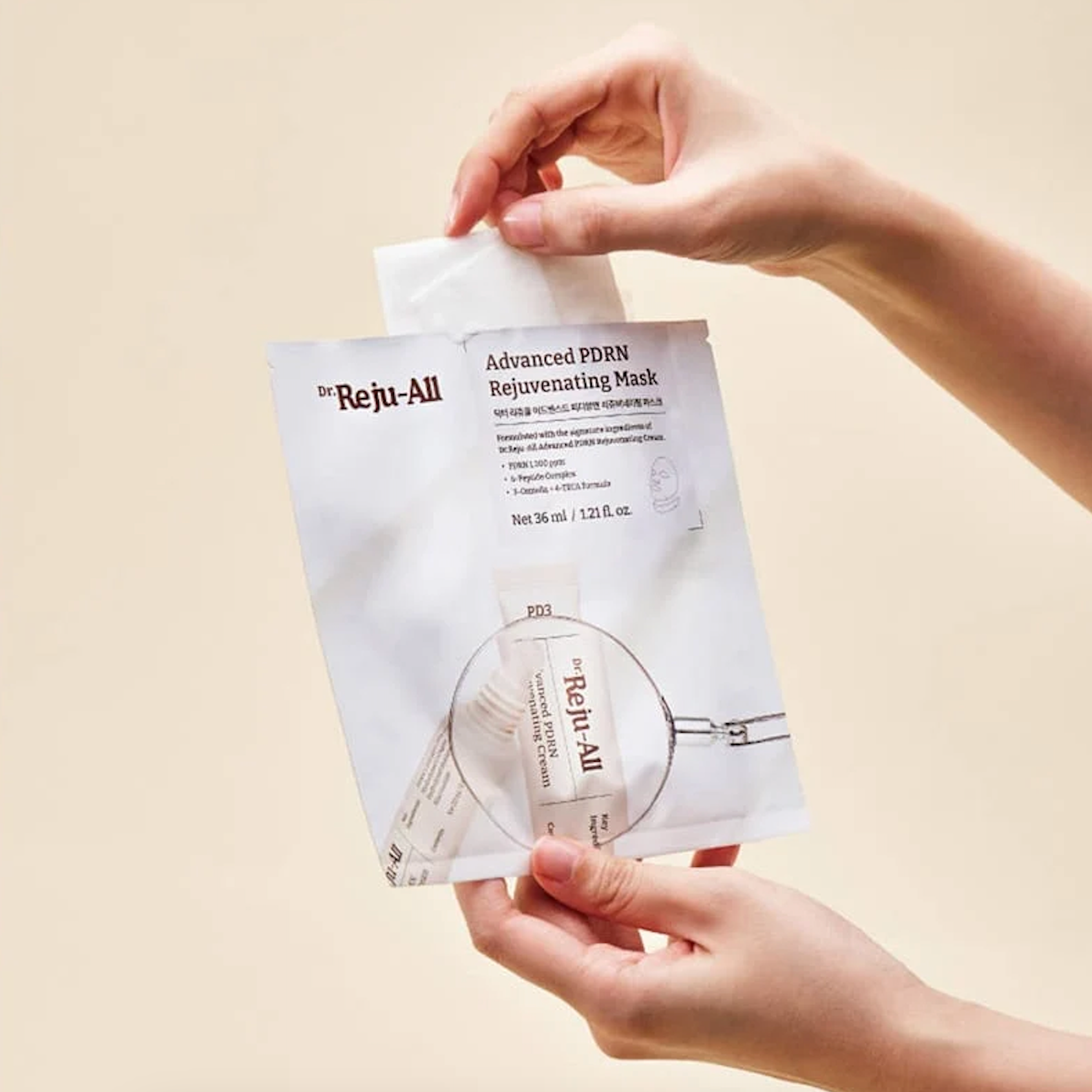 A person's hands holding and peeling back a white sheet from a Dr. Reji-All Advanced PDRN Rejuvenating Mask packet against a solid beige background.