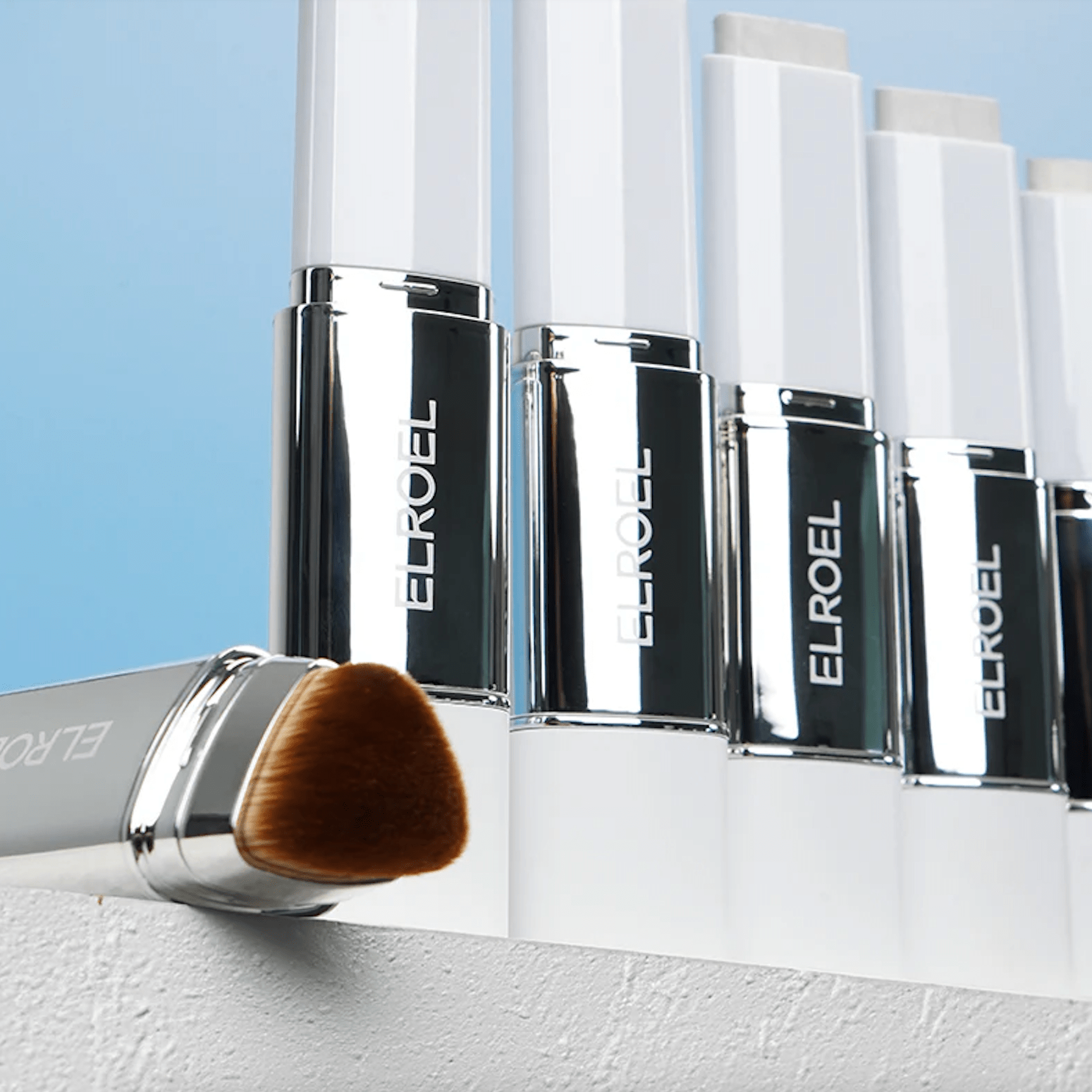 ELROEL Blanc Cover Cream Stick makeup products including bottles and a brush on a light blue background