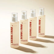 Four skincare pump bottles from K-SECRET SEOUL 1988 Essence Snail Mucin 97% + Rice arranged in a row on a warm beige background. The bottles are a warm cream color with bold red vertical text and clear caps.