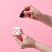 Hand holding a dropper over a K-SECRET Seoul 1988 Boosting Ball Collagen 100% against a pink background
