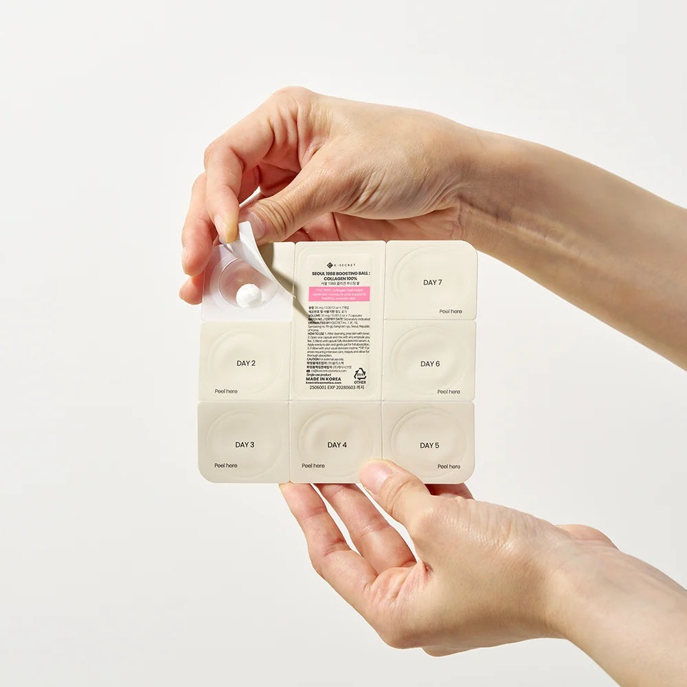 Hand holding a K-SECRET Seoul 1988 Boosting Ball Collagen 100% packaging with text on a white background