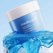 A blue and white jar of MEDICUBE Hyaluronic Ceramide Jelly Cream, styled with a splash of translucent blue gel at its base against a light blue background.