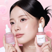 A close-up of a woman holding two Medikube skincare dropper bottles against a soft pink background with floating bubbles and text callouts describing hydrating and moisturizing textures.