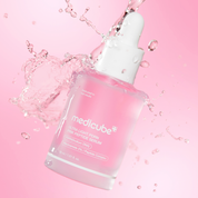 Medicube Ultra Light Firming Pink Peptide Serum in a frosted glass dropper bottle, surrounded by a dynamic water splash on a soft pink background.