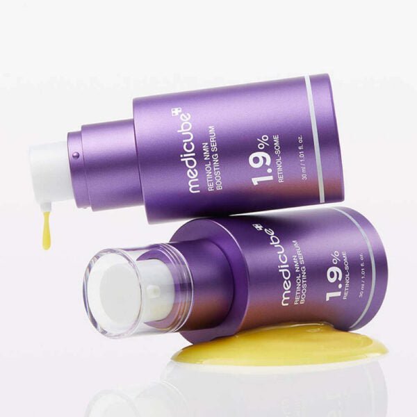 Two purple bottles of MEDICUBE Retinol NMN Boosting Serum with a yellow sponge on a white background