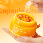 Yellow jar of Medicube KOJIC ACID TURMERIC VITA CAPSULE CREAM  with a hand holding a capsule against an orange background