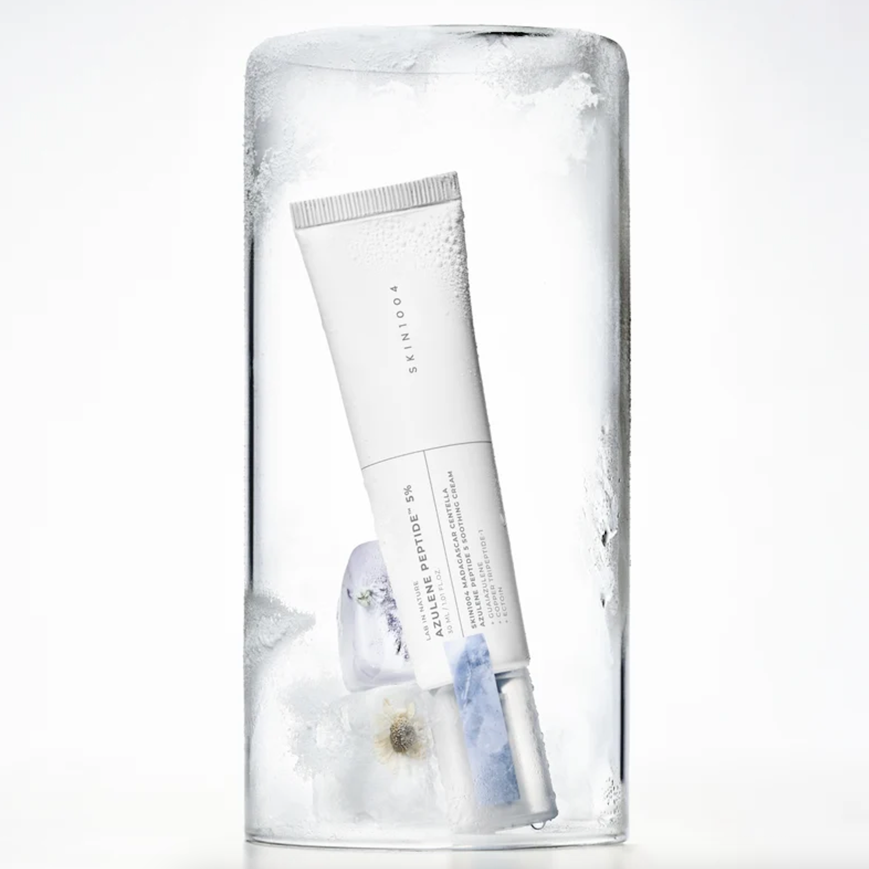 A white tube of SKIN1004 Madagascar Centella Azulene Peptide 5 Soothing Cream resting inside a clear cylindrical glass container filled with ice, on a white background.