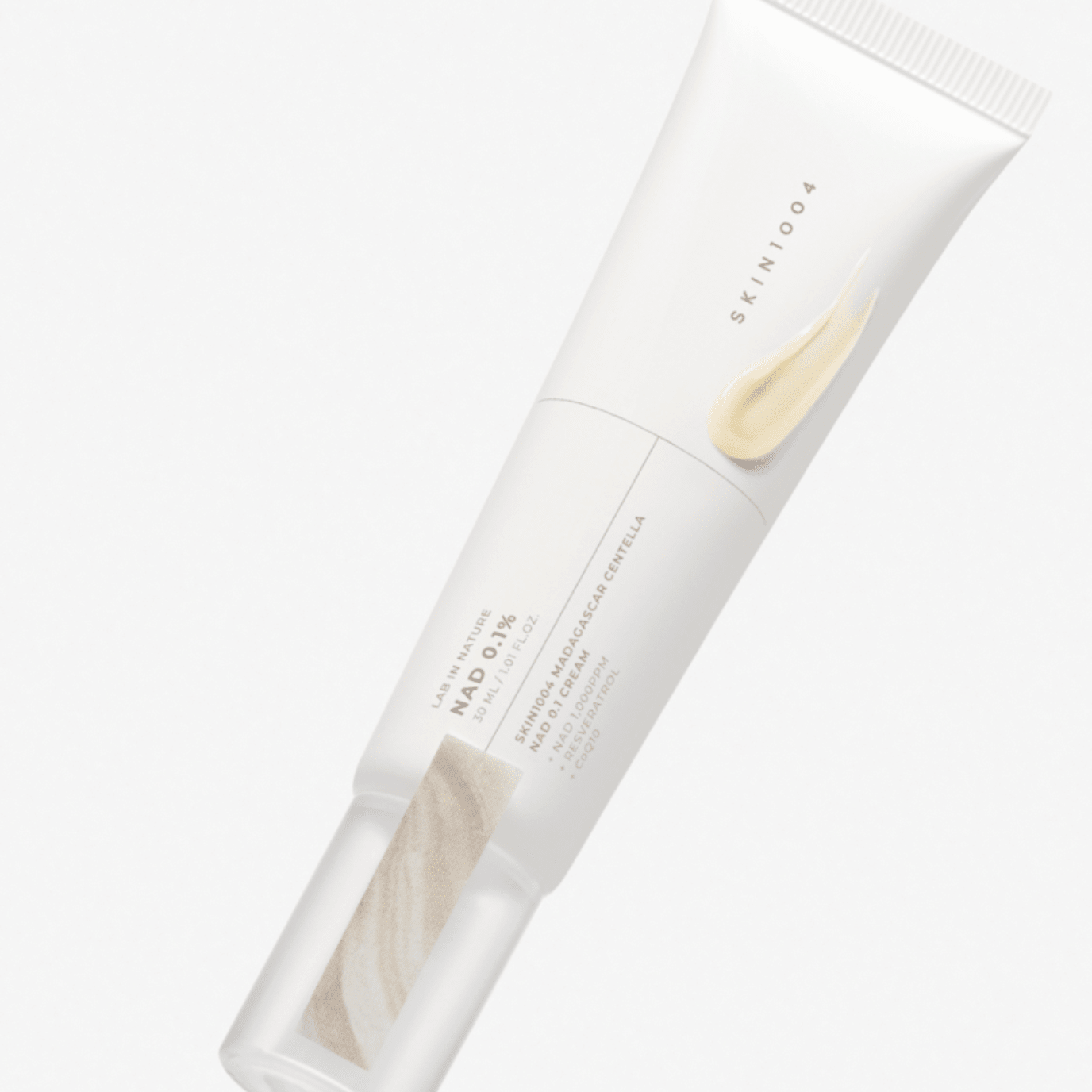 A white squeeze tube of SKIN1004 Madagascar Centella NAD 0.1 Cream, featuring a light beige cream smear graphic on the front, set against a clean white background.