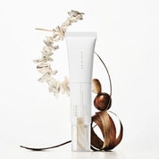 A white squeeze tube of SKIN1004 Madagascar Centella NAD 0.1 Cream with a clear cap, styled with dried white flowers and brown botanical elements on a clean white background.