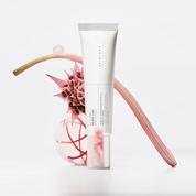 A white cosmetic tube labeled SKIN1004 Madagascar Centella PDRN 1.5 Cream stands upright on a white surface, styled with pink botanical props against a clean white background.
