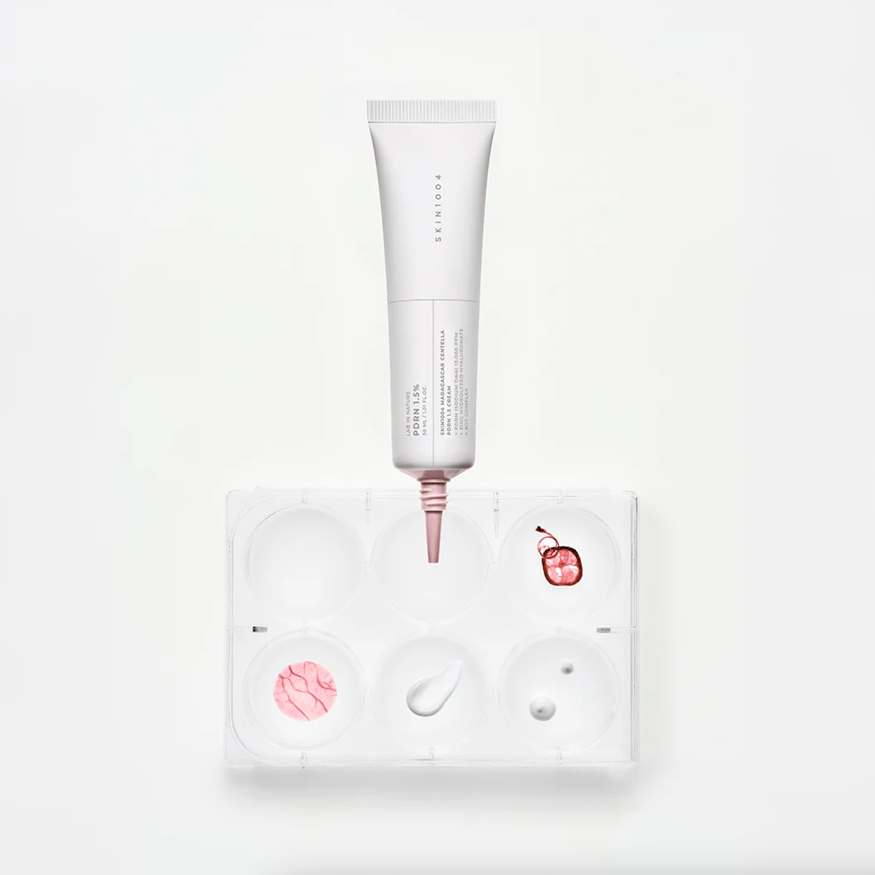 SKIN1004 Madagascar Centella PDRN 1.5 Cream tube with pink detailing is positioned above a white palette tray containing pink cream and a white cream swatch, on a clean white background.