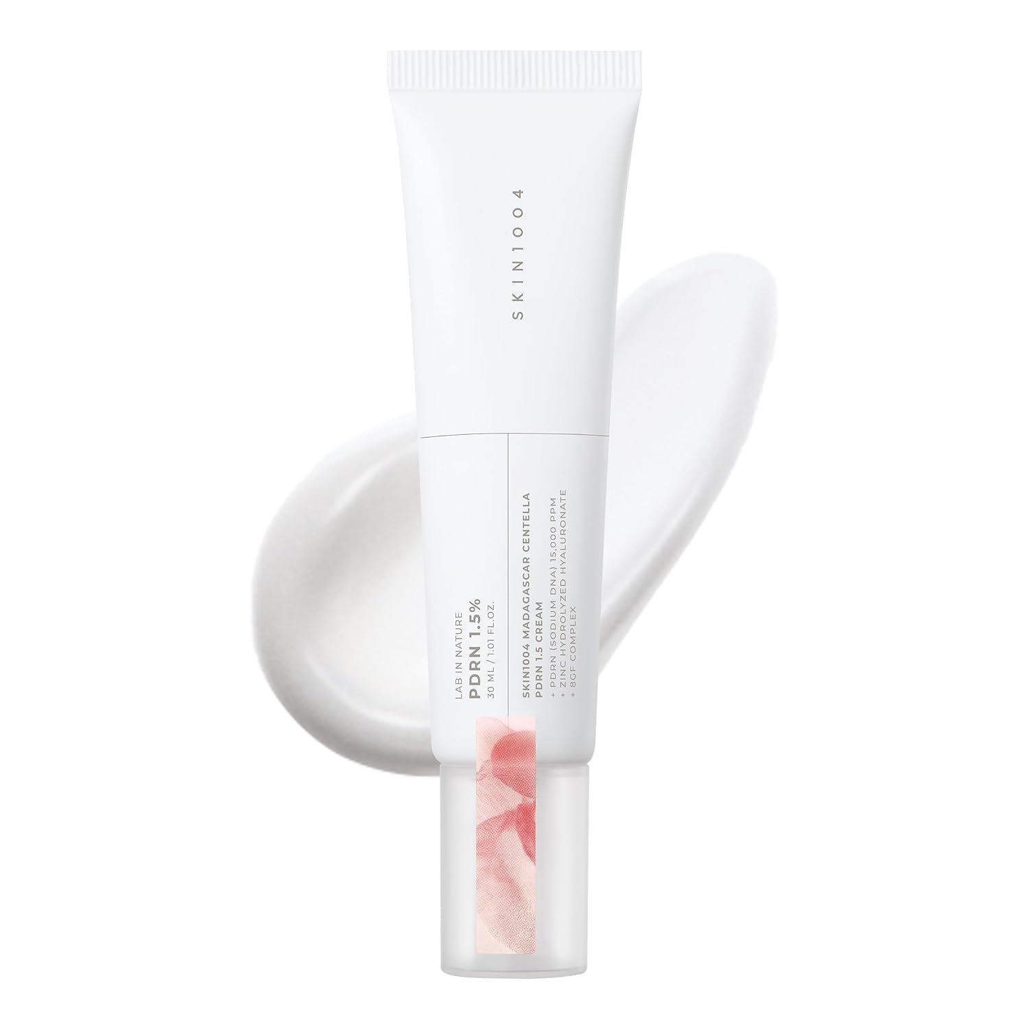 A white squeeze tube of SKIN1004 Madagascar Centella PDRN 1.5 Cream with a clear cap showing pink liquid, set against a white background with a soft pink product smear behind it.