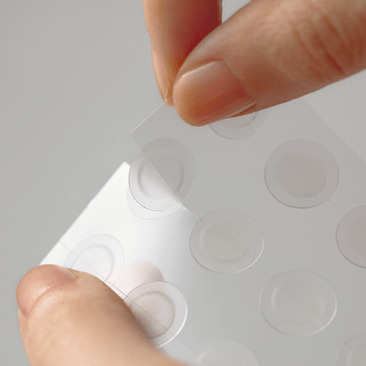 Hand holding a sheet of clear adhesive dots against a gray background
