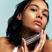 Woman holding a VT COSMETICS PDRN Essence 100 against a light blue background