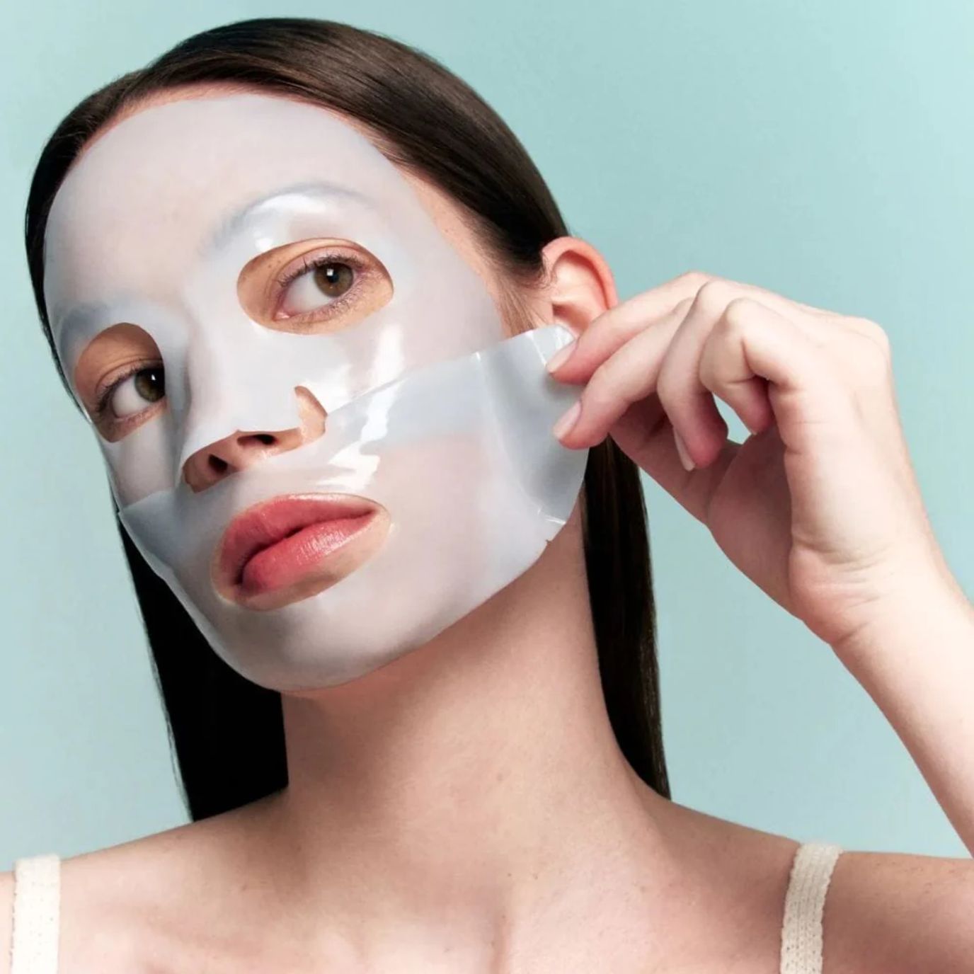 Woman applying a VT COSMETICS PDRN Hydrogel Mask against a light blue background