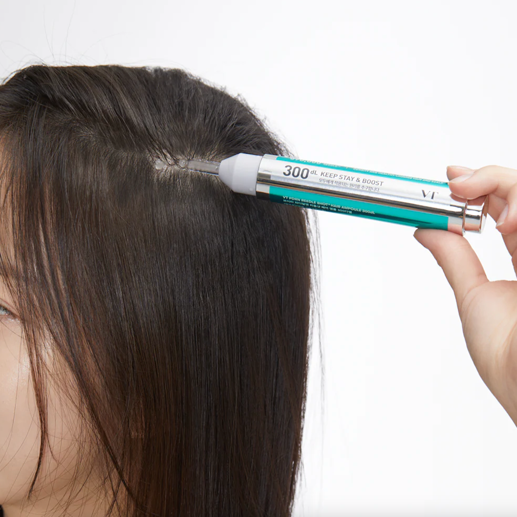 Person applying a hair product labeled VT COSMETICS PDRN Reedle Shot Hair Ampoule 300DL to their hair on a white background