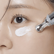 Close-up of a woman applying VT COSMETICS PDRN Reedle Shot Eye Lifter cream to her face with a dropper.